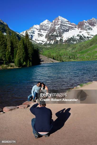 Visitors pose for photographs beside Maroon Lake. Maroon Lake and the Maroon Bells in the background are popular outdoor recreation destinations near...