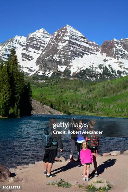 Hikers pose for photographs beside Maroon Lake. Maroon Lake and the Maroon Bells in the background are popular outdoor recreation destinations near...