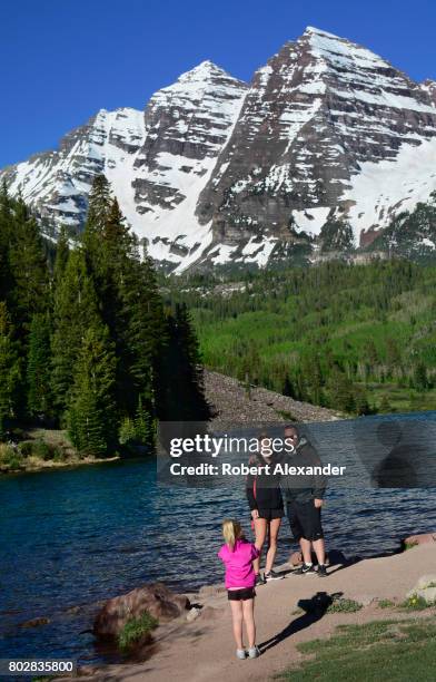 Young girl takes a souvenir photograph of her parents standing beside Maroon Lake. Maroon Lake and the Maroon Bells in the background are popular...