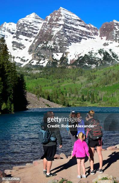 Hikers pose for photographs beside Maroon Lake. Maroon Lake and the Maroon Bells in the background are popular outdoor recreation destinations near...