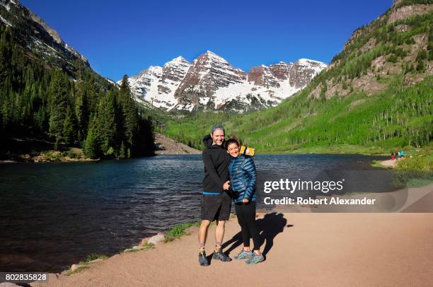 Couple takes a 'selfie' photograph beside Maroon Lake. Maroon Lake and the Maroon Bells in the background are popular outdoor recreation destinations...