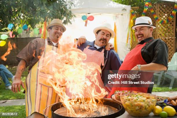 hispanic men leaning back from fire in barbecue grill - action cooking fotografías e imágenes de stock