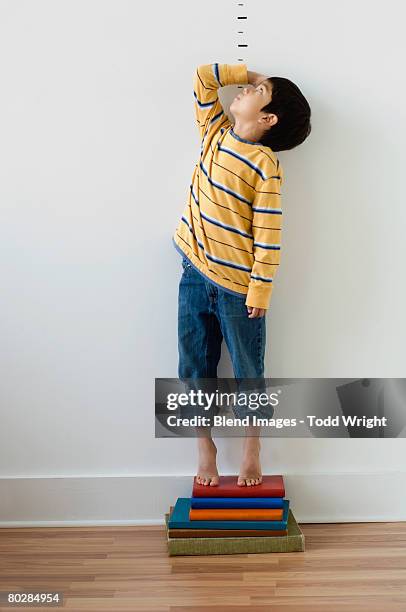asian boy standing on books in front of height markers - lengte stockfoto's en -beelden
