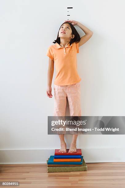 asian girl standing on books in front of height markers - height ストックフォトと画像