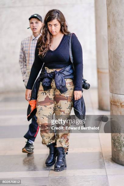Guest wears a black low neck top, military camouflage print pants, black boots, outside the 22/4 Hommes show, during Paris Fashion Week - Menswear...