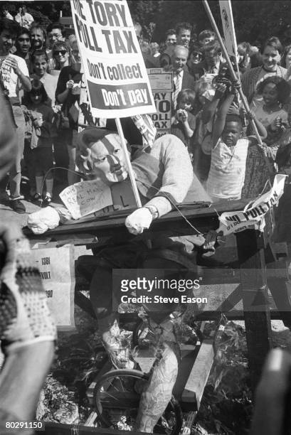 Anti-poll tax campaign directed against Prime Minister Margaret Thatcher, an effigy of whom is being pilloried, 27th May 1990. A placard reads 'The...