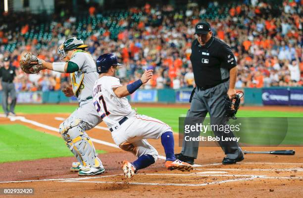 Jose Altuve of the Houston Astros slides safely at home as Bruce Maxwell of the Oakland Athletics is unable to cleanly handle the ball as home plate...