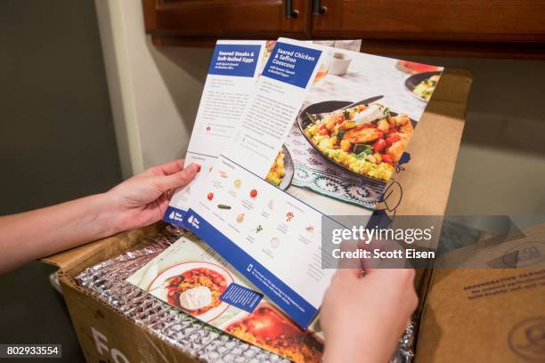 In this photo illustration, a Blue Apron customer looks at recipes for the weeks meals from inside a Blue Apron box on a kitchen counter on June 28,...
