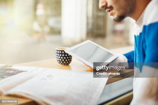 lächelnder junge mann mit digital-tablette im café - junger mann liest zeitung stock-fotos und bilder