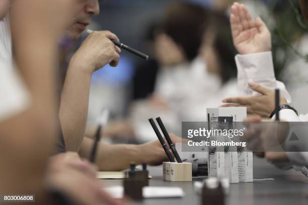Japan Tobacco Inc.'s Ploom Tech smokeless tobacco devices sit on display while an attendee tries them out at the company's Ploom Shop Ginza in Tokyo,...