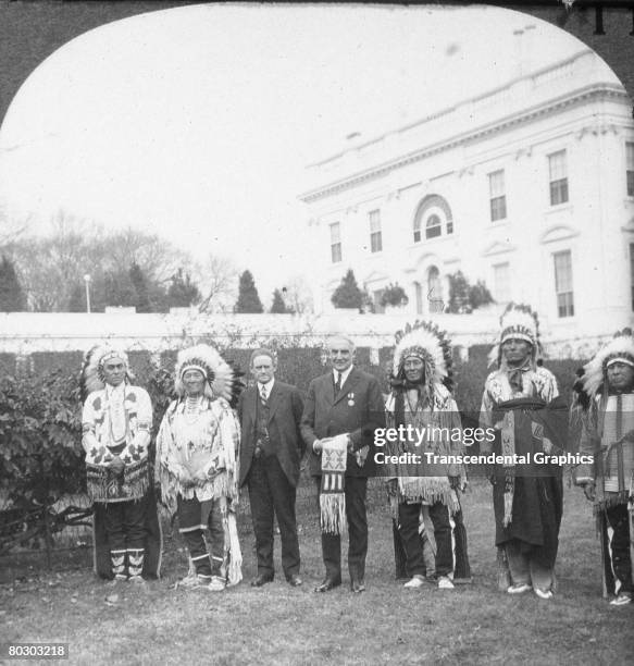 On the grounds of the White House, American President Warren G. Harding and Commissioner of the Bureau of Indian Affairs Charles Henry Burke pose...