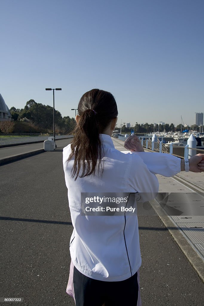 Woman stretching at pier, rear view