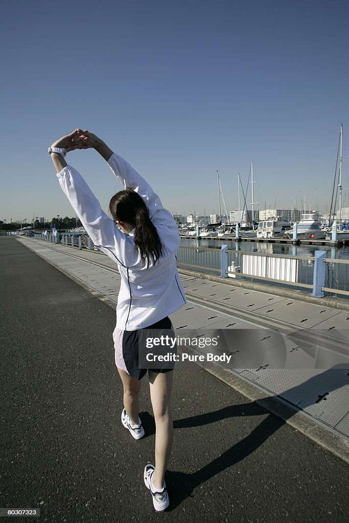 Woman stretching at pier, rear view