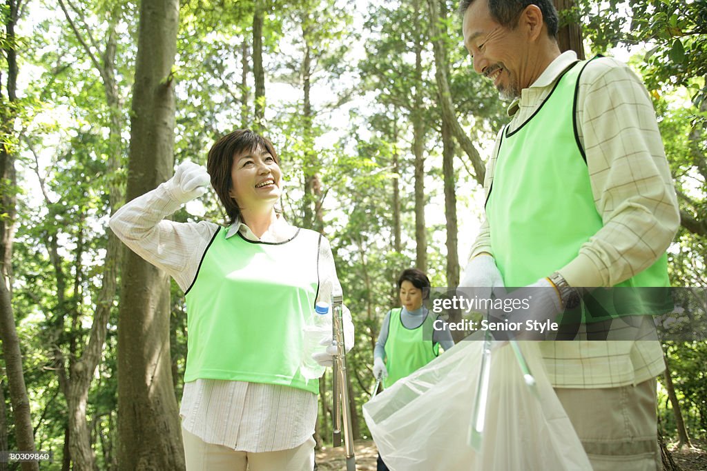 Three mature adults cleaning up trash in park