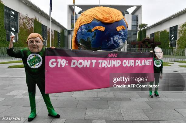 Activists wearing masks of German Chancellor Angela Merkel and the President of the European Commission Jean-Claude Juncker hold up a banner reading...