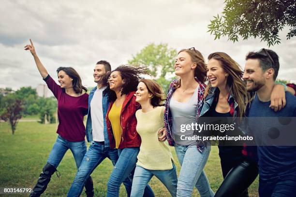 happy friends are wlaking ahead arm in arm - community arm in arm stock pictures, royalty-free photos & images