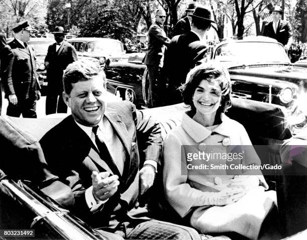 President John F Kennedy and Jacqueline Kennedy smile while sitting in the back seat of an open car, John Kennedy pointing towards the camera, May 3,...