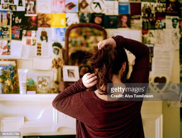 back of teenage girl in bedroom, looking in mirror and doing her hair - girls in bedroom stock-fotos und bilder