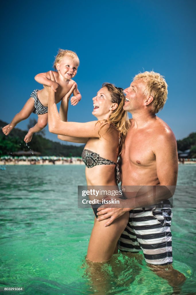 Felice ritratto di famiglia: giovane coppia con bambino in vacanza. Cielo azzurro chiaro, acqua azzurra, felicità