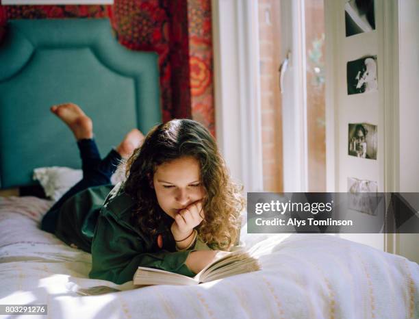 teenage girl lying on her bed, reading a book - leggere foto e immagini stock