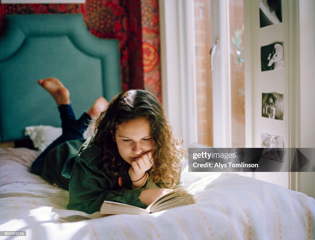 Teenage girl lying on her bed, reading a book