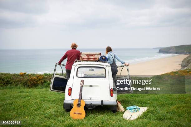hipster couple on road trip overlooking sea. - car-door stock pictures, royalty-free photos & images