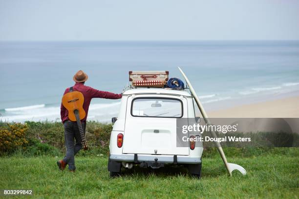 hipster man on road trip with guitar and surfboard. - car rear stock-fotos und bilder