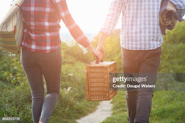 couple carrying picnic hamper on coastal path. - romantic picnic stockfoto's en -beelden