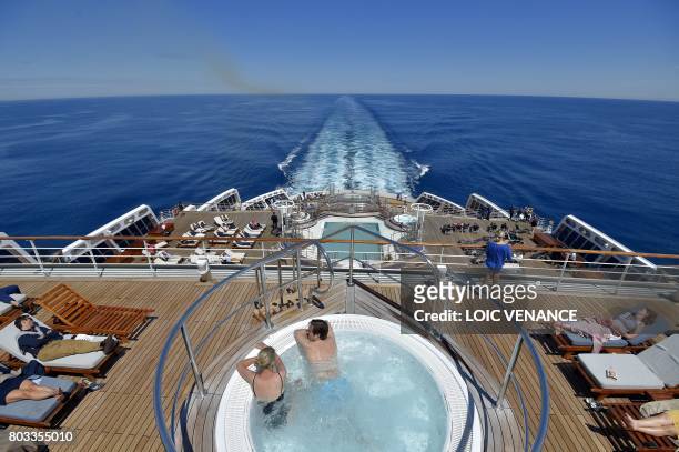 People sunbath while a couple has a swim aboard of the Cunard cruise liner RMS Queen Mary 2 sailing in the Atlantic ocean, on June 28 during The...