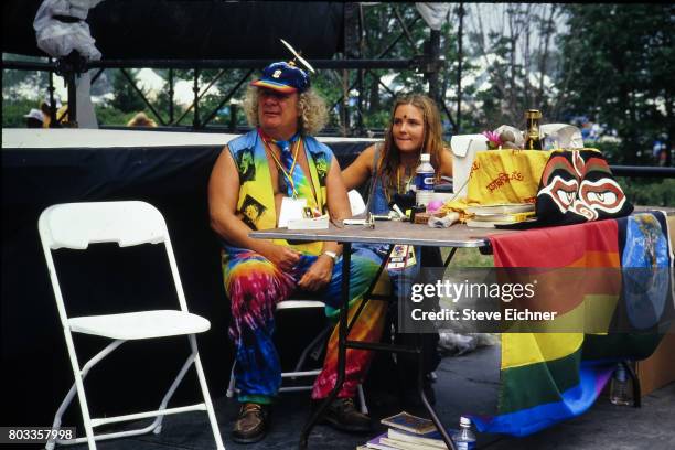 View of Wavy Gravy , along with an unidentified woman, at a folding table at the Woodstock '94 festival, Saugerties, New York, August 14, 1994.