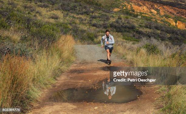 a young hiker runs and jumps over a puddle on a dirt road. - leap of faith stock pictures, royalty-free photos & images