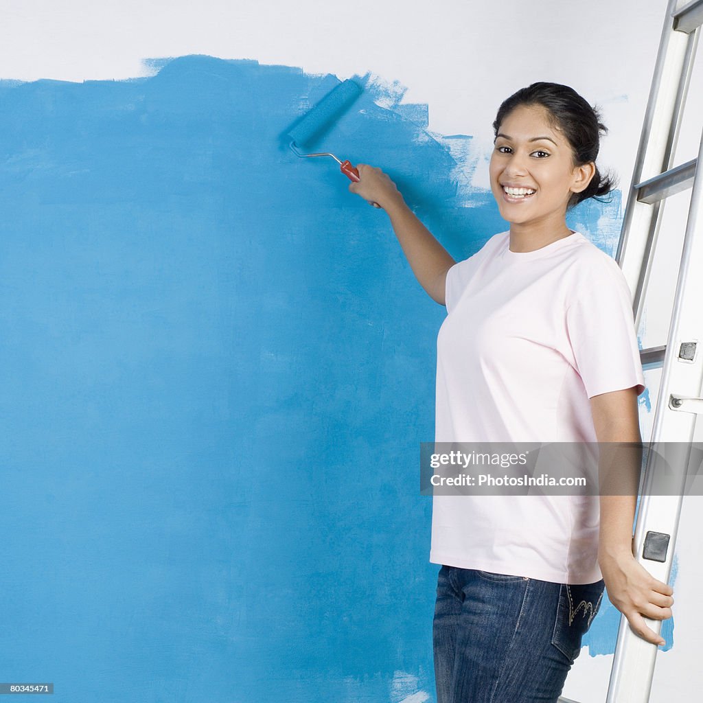 Portrait of a young woman painting a wall with a paint roller