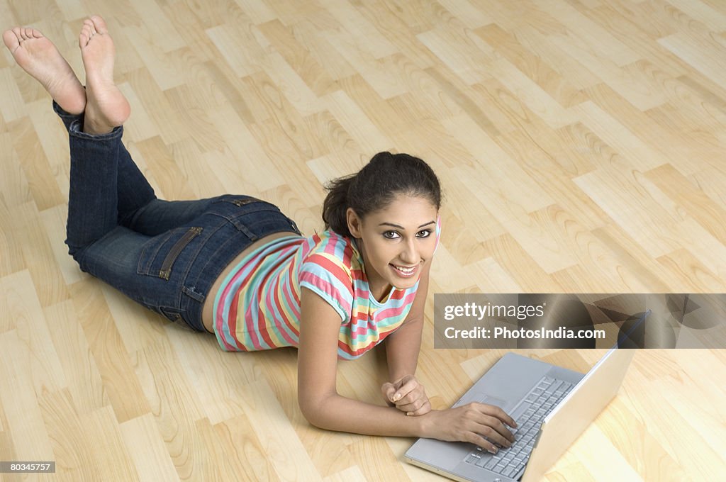 Portrait of a young woman lying on the floor and using a laptop