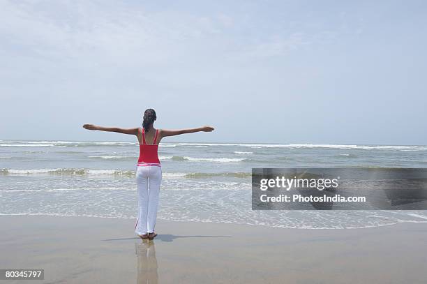 rear view of a young woman standing on the beach with her arms outstretched - yoga goa woman stock pictures, royalty-free photos & images