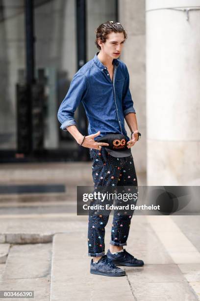 Guest wears a blue denim shirt, a black cap, pacman print pants, sneakers outside the 22/4 Hommes show, during Paris Fashion Week - Menswear...