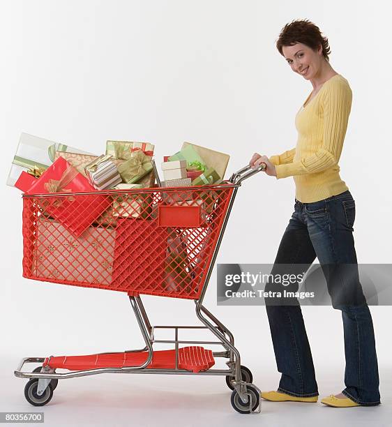 woman pushing shopping cart of gifts - mujeres de mediana edad fotografías e imágenes de stock
