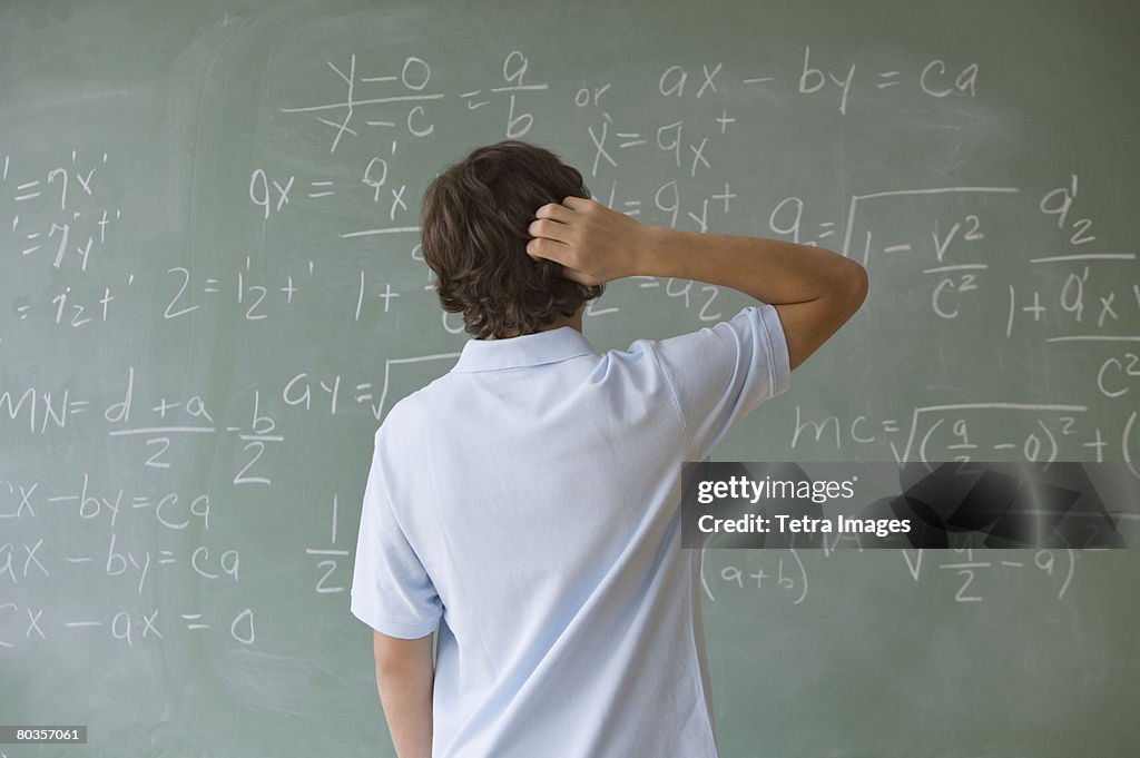 Teenaged boy looking at math equations on blackboard