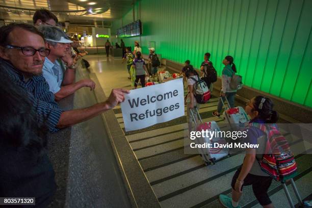 John Wider carries a welcome sign near arriving international travelers on the first day of the the partial reinstatement of the Trump travel ban,...