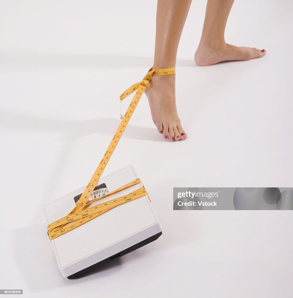 Woman's foot tied to scale with tape measure