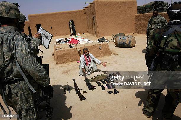 An Iraqi man gestures toward weapons found in his home as US soldiers from Ghostrider Company 3rd Squadron 2nd Stryker Cavalry Regiment prepare to...