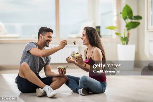 hombre feliz alimentando a su novia mientras estaba sentado en el piso en su ático nuevo. - sitting on floor fotografías e imágenes de stock