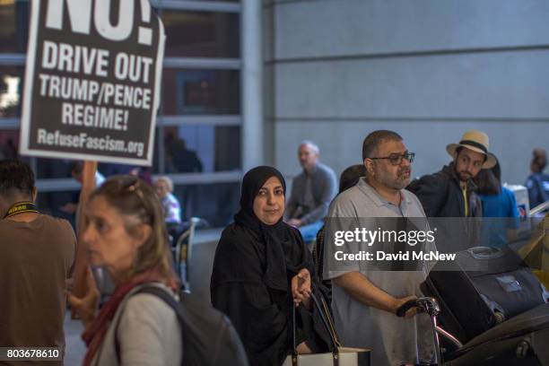 Arriving international travelers pass protesters on the first day of the the partial reinstatement of the Trump travel ban, temporarily barring...