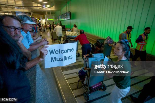 John Wider carries a welcome sign near arriving international travelers on the first day of the the partial reinstatement of the Trump travel ban,...