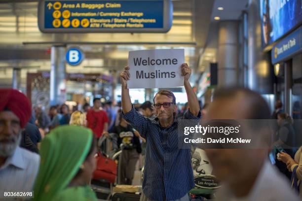 John Wider carries a welcome sign near arriving Sikh travelers on the first day of the the partial reinstatement of the Trump travel ban, temporarily...