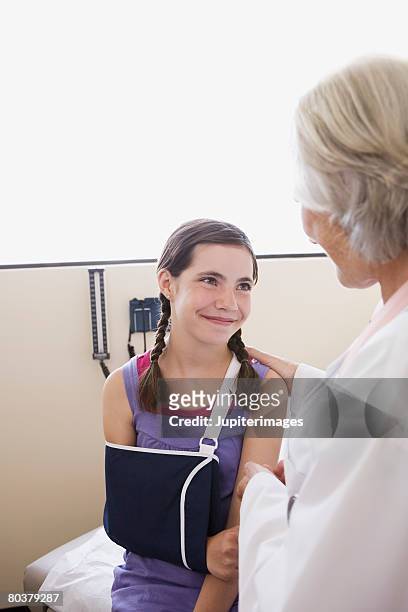 smiling preteen girl wearing sling with doctor - kind mit armschlinge stock-fotos und bilder