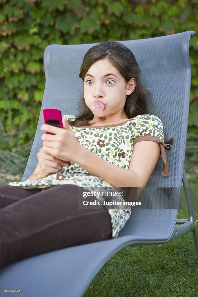 Preteen girl blowing gum bubble and texting