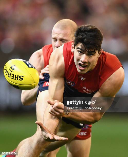 Christian Petracca of the Demons handballs whilst being tackled by Zak Jones of the Swans during the round 15 AFL match between the Melbourne Demons...