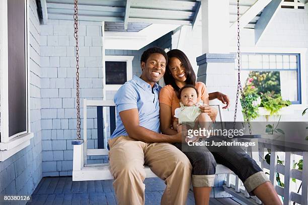 smiling family seated on porch swing - hollywoodschaukel stock-fotos und bilder
