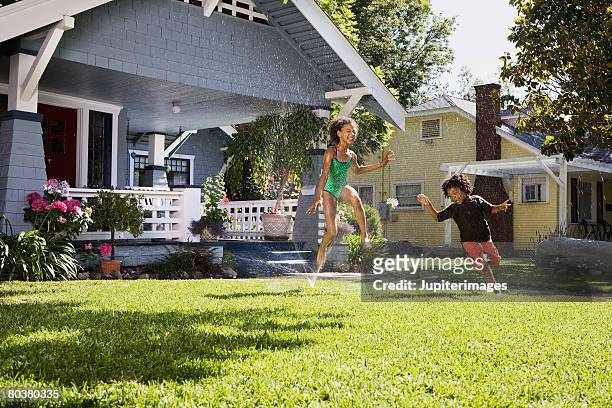 children playing in front lawn sprinkler - front lawn stock pictures, royalty-free photos & images
