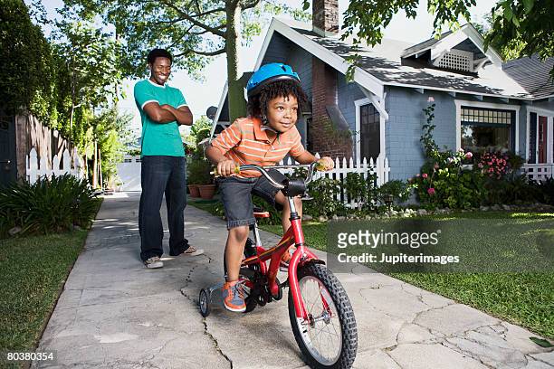father teaching boy to ride bicycle - stützrad stock-fotos und bilder